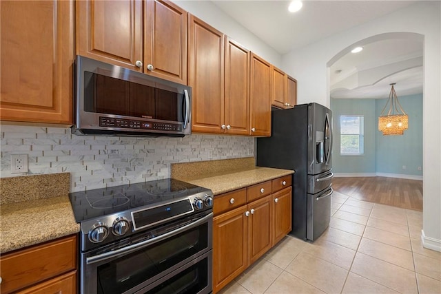 kitchen featuring appliances with stainless steel finishes, tasteful backsplash, light stone counters, and light tile patterned flooring