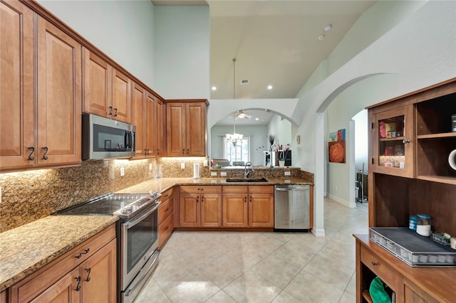 kitchen with light stone counters, stainless steel appliances, a notable chandelier, high vaulted ceiling, and sink