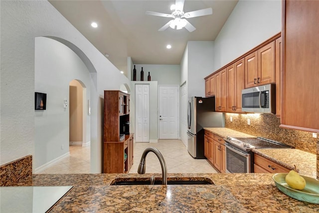 kitchen with sink, ceiling fan, dark stone counters, appliances with stainless steel finishes, and decorative backsplash