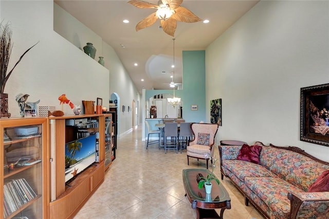 tiled living room with a towering ceiling and ceiling fan with notable chandelier