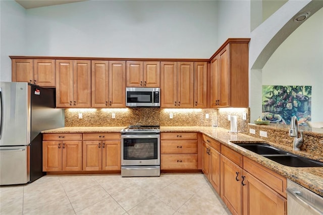 kitchen with appliances with stainless steel finishes, a high ceiling, light stone countertops, backsplash, and sink