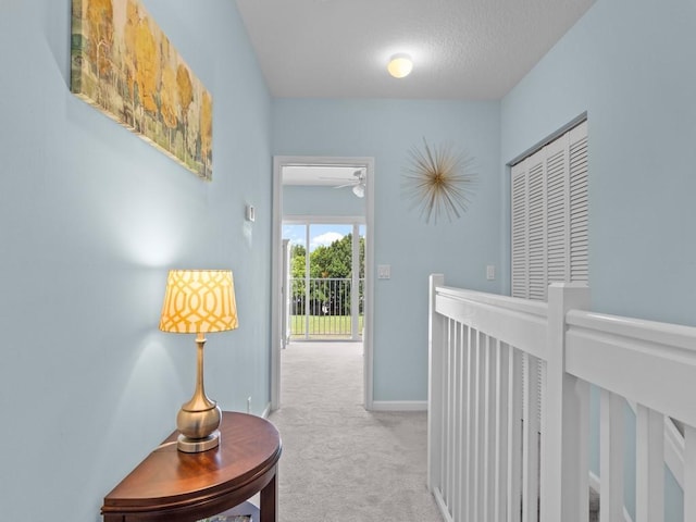 hallway featuring an upstairs landing, a textured ceiling, baseboards, and carpet floors