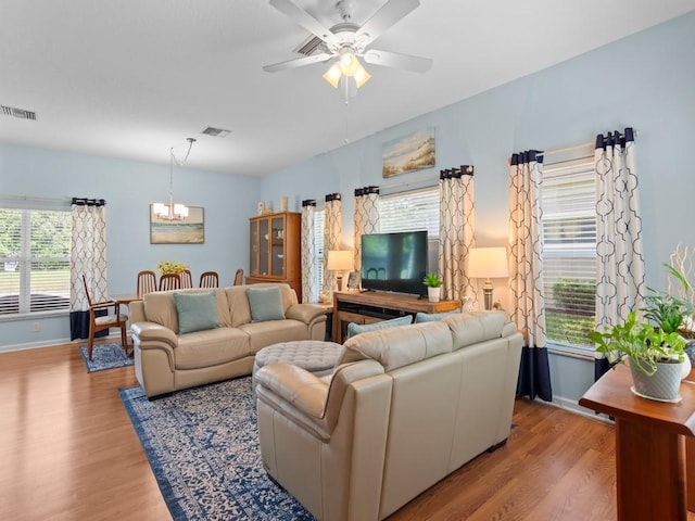 living room featuring plenty of natural light, ceiling fan with notable chandelier, and light wood-type flooring