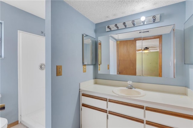 bathroom with a textured ceiling, walk in shower, ceiling fan, toilet, and vanity