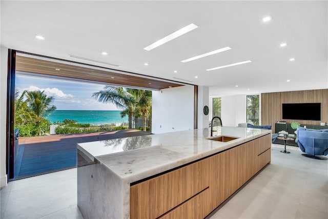 kitchen featuring modern cabinets, open floor plan, light stone countertops, concrete floors, and a sink