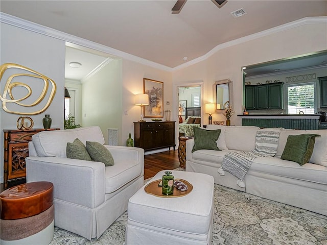 living area with visible vents, lofted ceiling, wood finished floors, and crown molding