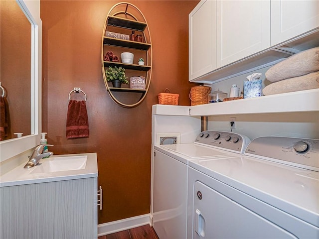 clothes washing area with dark wood-type flooring, a sink, washer and dryer, cabinet space, and baseboards