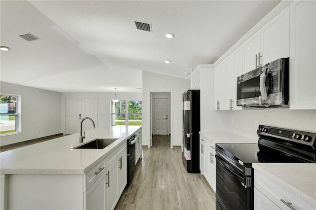 kitchen featuring vaulted ceiling, white cabinetry, sink, black appliances, and a center island with sink