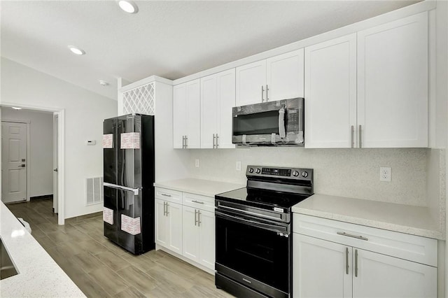 kitchen featuring vaulted ceiling, appliances with stainless steel finishes, white cabinetry, decorative backsplash, and light wood-type flooring