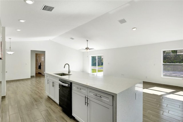 kitchen featuring pendant lighting, sink, lofted ceiling, black dishwasher, and a center island with sink