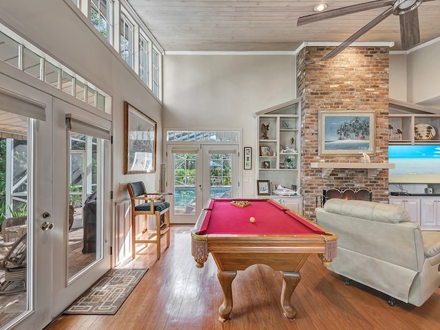 recreation room with a wealth of natural light, a towering ceiling, light wood-type flooring, and french doors