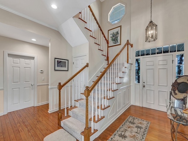 foyer entrance featuring ornamental molding, light hardwood / wood-style flooring, vaulted ceiling, and an inviting chandelier