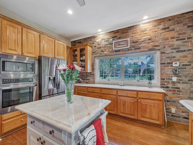 kitchen with brick wall, light hardwood / wood-style flooring, appliances with stainless steel finishes, and a center island