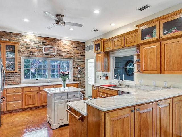 kitchen with light stone counters, a kitchen island, light hardwood / wood-style floors, kitchen peninsula, and brick wall