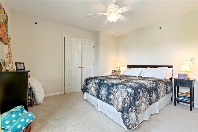 bedroom featuring light colored carpet, ceiling fan, and a closet