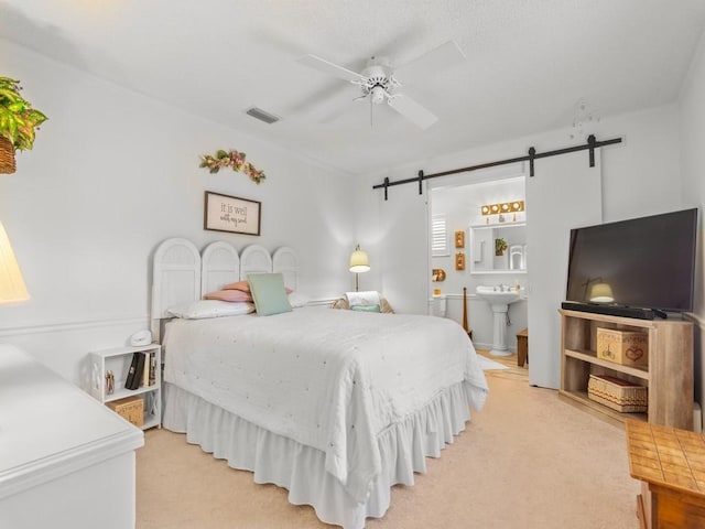 bedroom featuring light carpet, a barn door, visible vents, and a sink