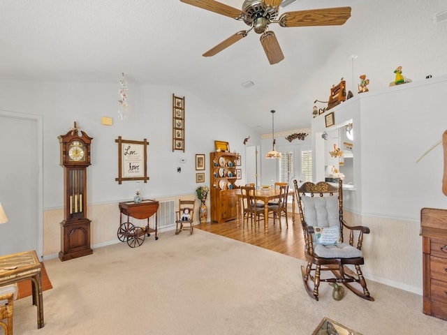 sitting room featuring visible vents, a ceiling fan, lofted ceiling, a wainscoted wall, and carpet flooring