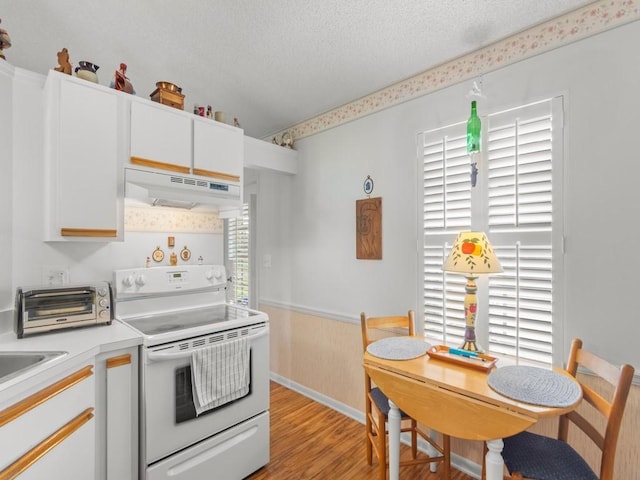 kitchen featuring a textured ceiling, under cabinet range hood, electric stove, wainscoting, and a wealth of natural light