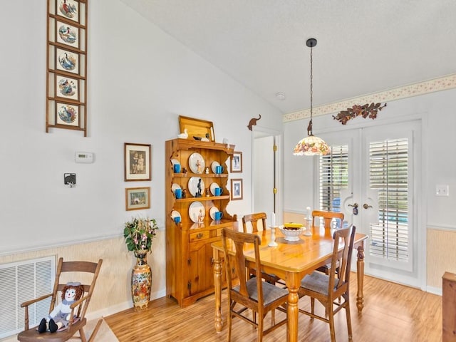 dining room with lofted ceiling, light wood finished floors, wainscoting, and visible vents