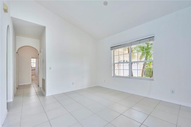 unfurnished room with light tile patterned floors, arched walkways, and vaulted ceiling