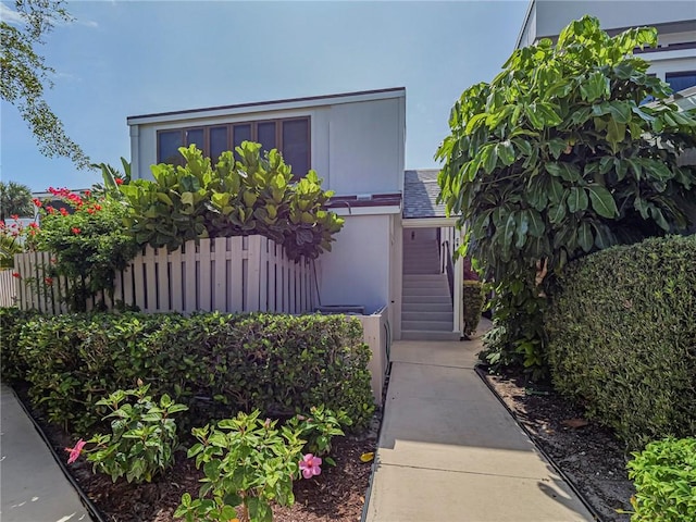 doorway to property with stucco siding, fence, and roof with shingles