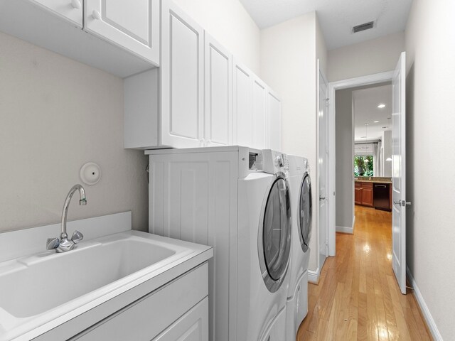 laundry area featuring light wood-type flooring, cabinets, sink, and washing machine and clothes dryer