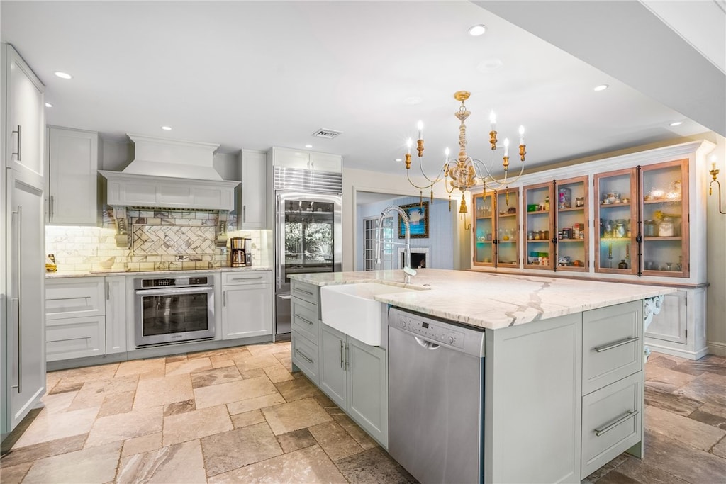 kitchen featuring sink, backsplash, a spacious island, custom range hood, and appliances with stainless steel finishes