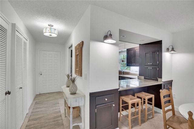 kitchen featuring kitchen peninsula, a textured ceiling, a breakfast bar, light tile patterned flooring, and dark brown cabinets