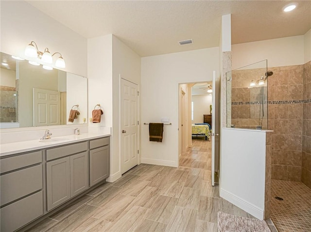 bathroom with a tile shower, vanity, and ceiling fan