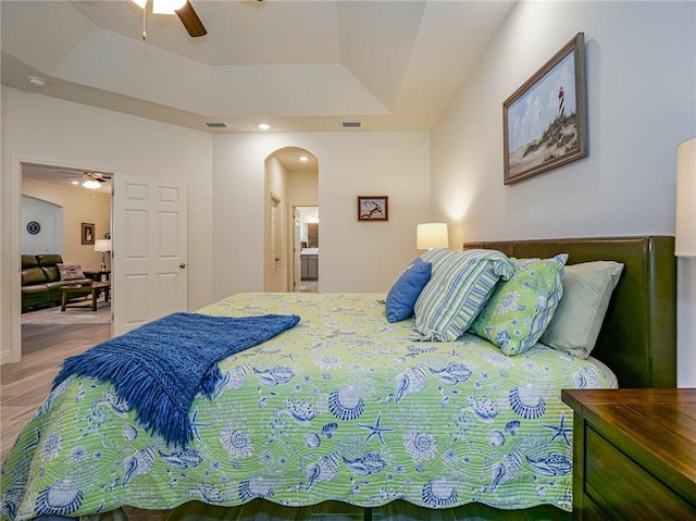 bedroom featuring connected bathroom, a raised ceiling, and ceiling fan