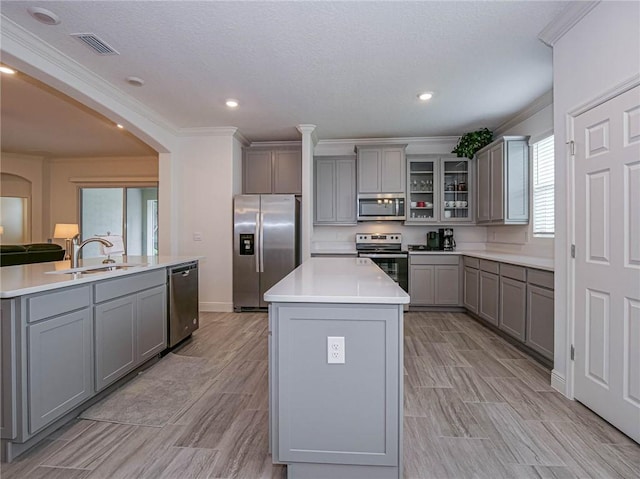 kitchen with ornamental molding, stainless steel appliances, a kitchen island with sink, sink, and gray cabinets