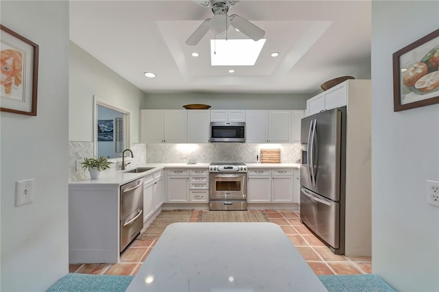 kitchen with stainless steel appliances, white cabinetry, tasteful backsplash, and a tray ceiling