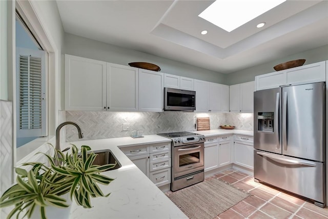 kitchen with a skylight, appliances with stainless steel finishes, a tray ceiling, white cabinets, and backsplash