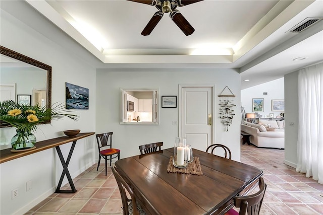 tiled dining area with ceiling fan and a tray ceiling