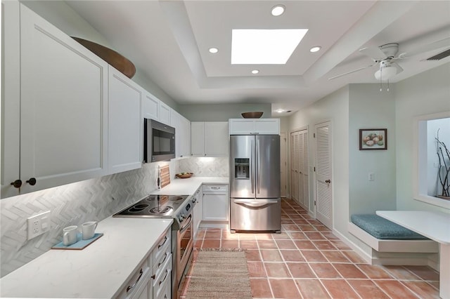 kitchen featuring white cabinetry, tasteful backsplash, a skylight, appliances with stainless steel finishes, and a tray ceiling