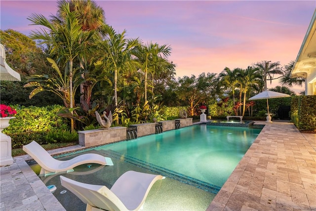 pool at dusk featuring an in ground hot tub and a patio