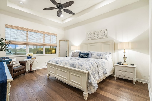 bedroom with dark hardwood / wood-style flooring, ceiling fan, and a raised ceiling