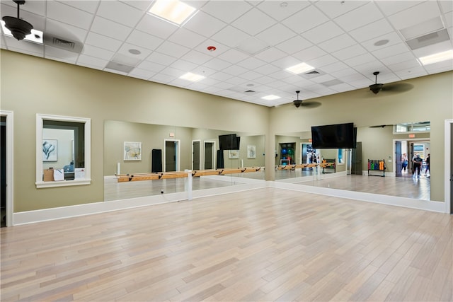 exercise area with light wood-type flooring, a paneled ceiling, and a high ceiling