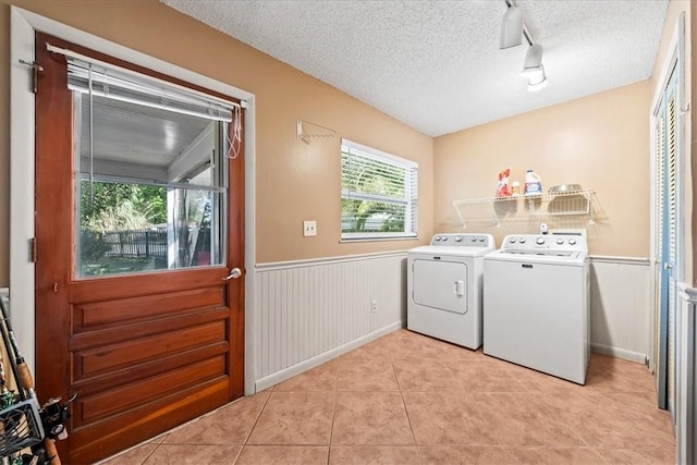 laundry area featuring light tile patterned floors, laundry area, a wainscoted wall, washing machine and clothes dryer, and a textured ceiling