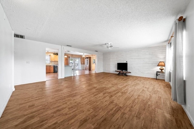 unfurnished living room with a textured ceiling, ceiling fan with notable chandelier, wood finished floors, visible vents, and baseboards