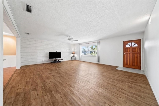 unfurnished living room with ceiling fan, a textured ceiling, visible vents, and wood finished floors