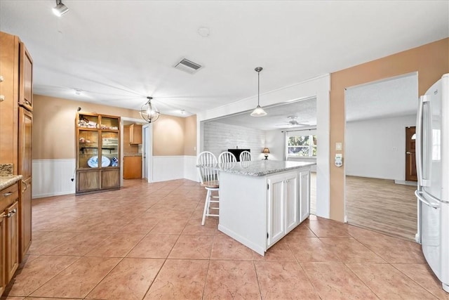 kitchen featuring visible vents, wainscoting, open floor plan, freestanding refrigerator, and light tile patterned flooring