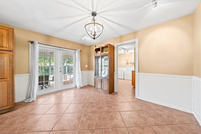 unfurnished dining area featuring light tile patterned floors, a notable chandelier, separate washer and dryer, french doors, and wainscoting