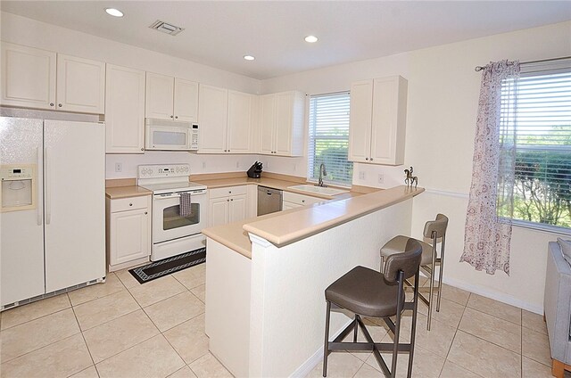 kitchen with white cabinetry, white appliances, light tile patterned floors, a breakfast bar, and kitchen peninsula