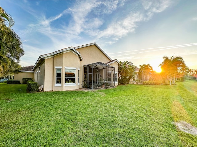 back of property at dusk featuring a lanai, a yard, and stucco siding