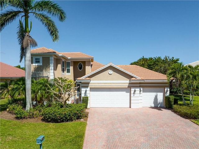 mediterranean / spanish house featuring a garage, a front lawn, decorative driveway, and stucco siding