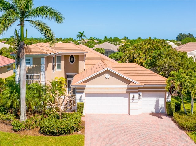 mediterranean / spanish home with a garage, a tiled roof, decorative driveway, and stucco siding