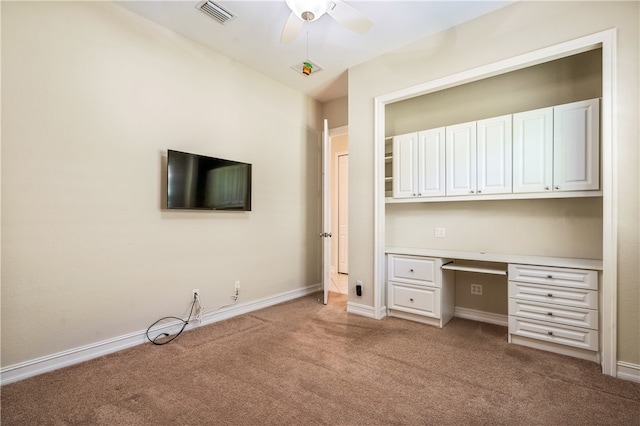 unfurnished office with built in desk, ceiling fan, and light carpet