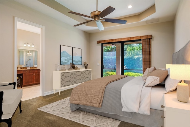 carpeted bedroom featuring a raised ceiling, ceiling fan, and ensuite bath