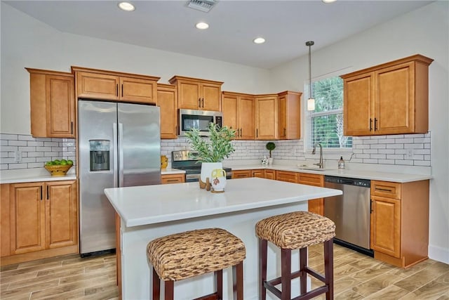 kitchen with a kitchen bar, sink, a center island, hanging light fixtures, and stainless steel appliances